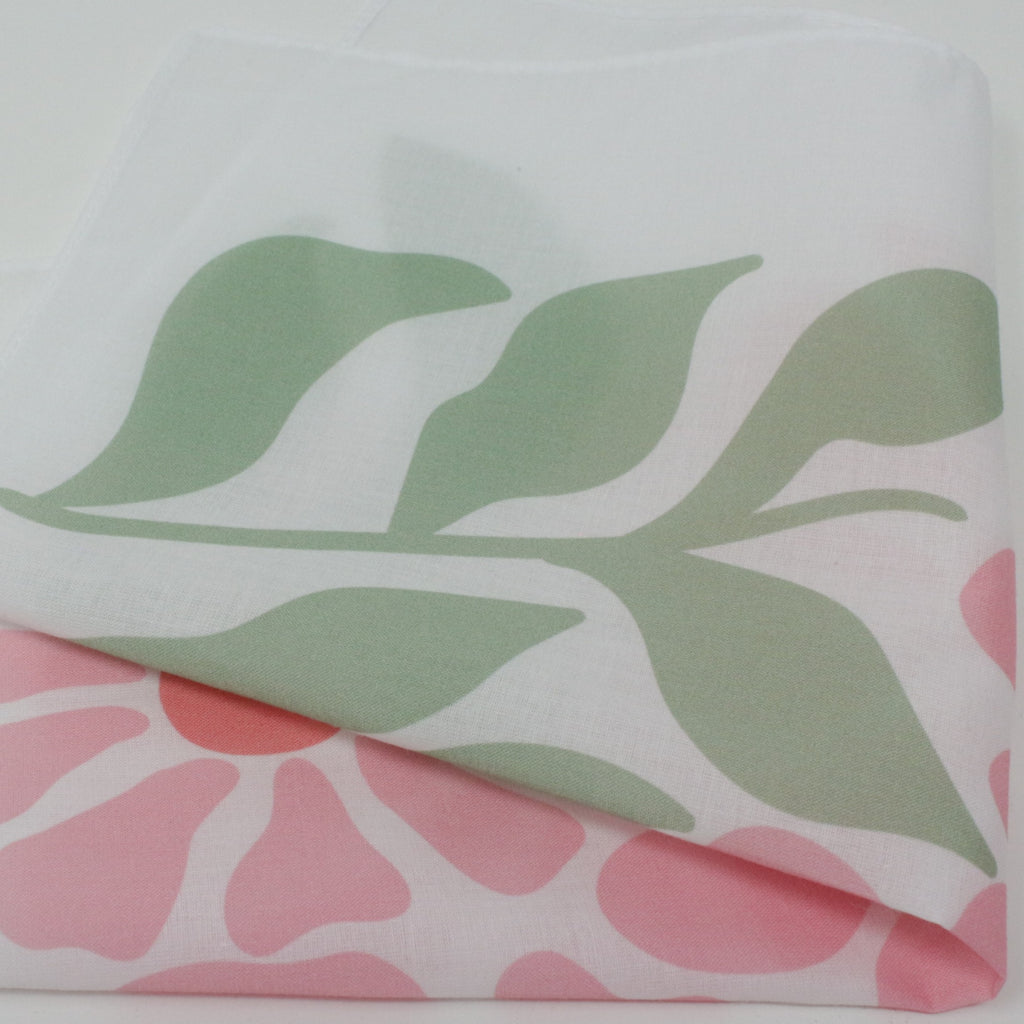 A folded white fabric handkerchief, featuring a large sage green leaf pattern on the top layer and a pink floral pattern on the bottom layer.
