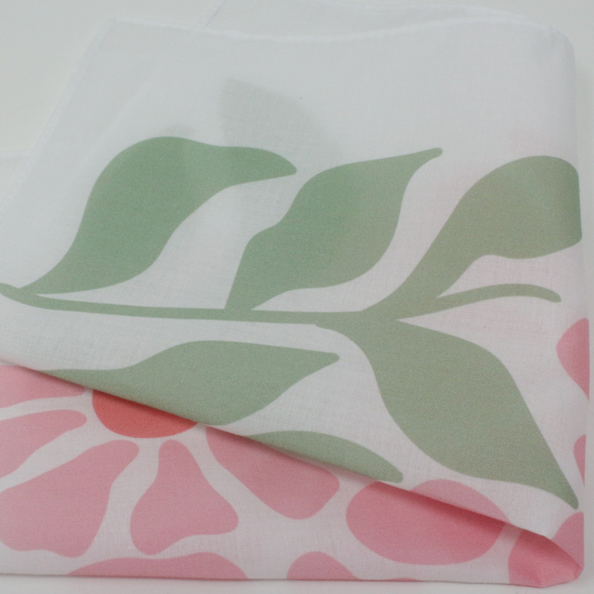 A folded white fabric handkerchief, featuring a large sage green leaf pattern on the top layer and a pink floral pattern on the bottom layer.