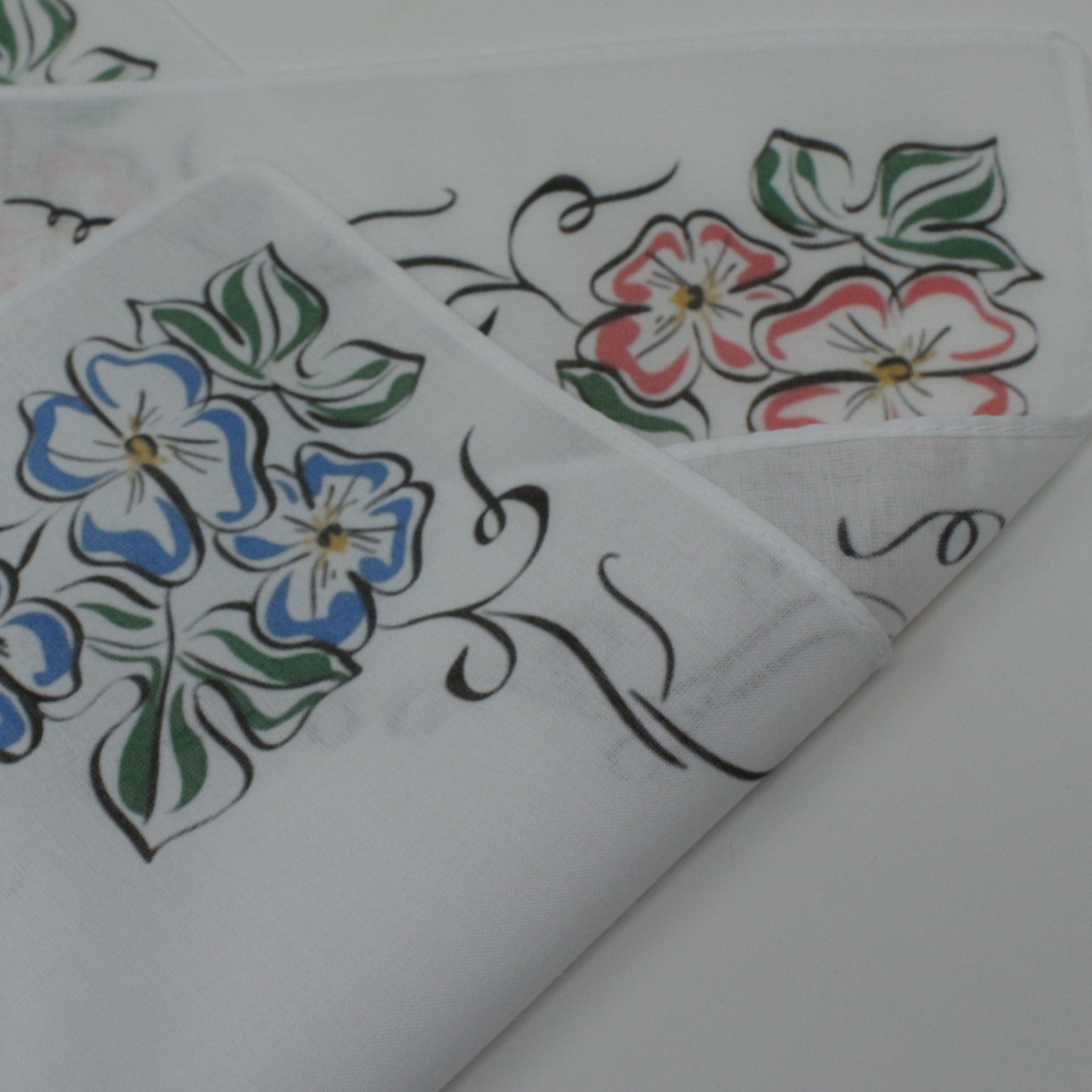 A folded white fabric cotton handkerchief with embroidered floral patterns, including blue flowers, pink flowers, green leaves, and black scroll details.