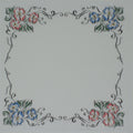A square white cotton handkierchief, decorative floral border design in the corners, with pink and blue flowers, green leaves, and black scrollwork.
