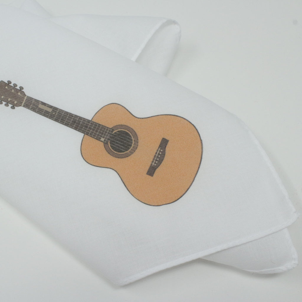 A folded white fabric item, likely a cotton hankie, printed with a graphic of an acoustic guitar in natural wood tones and black details, set against a clean white background.