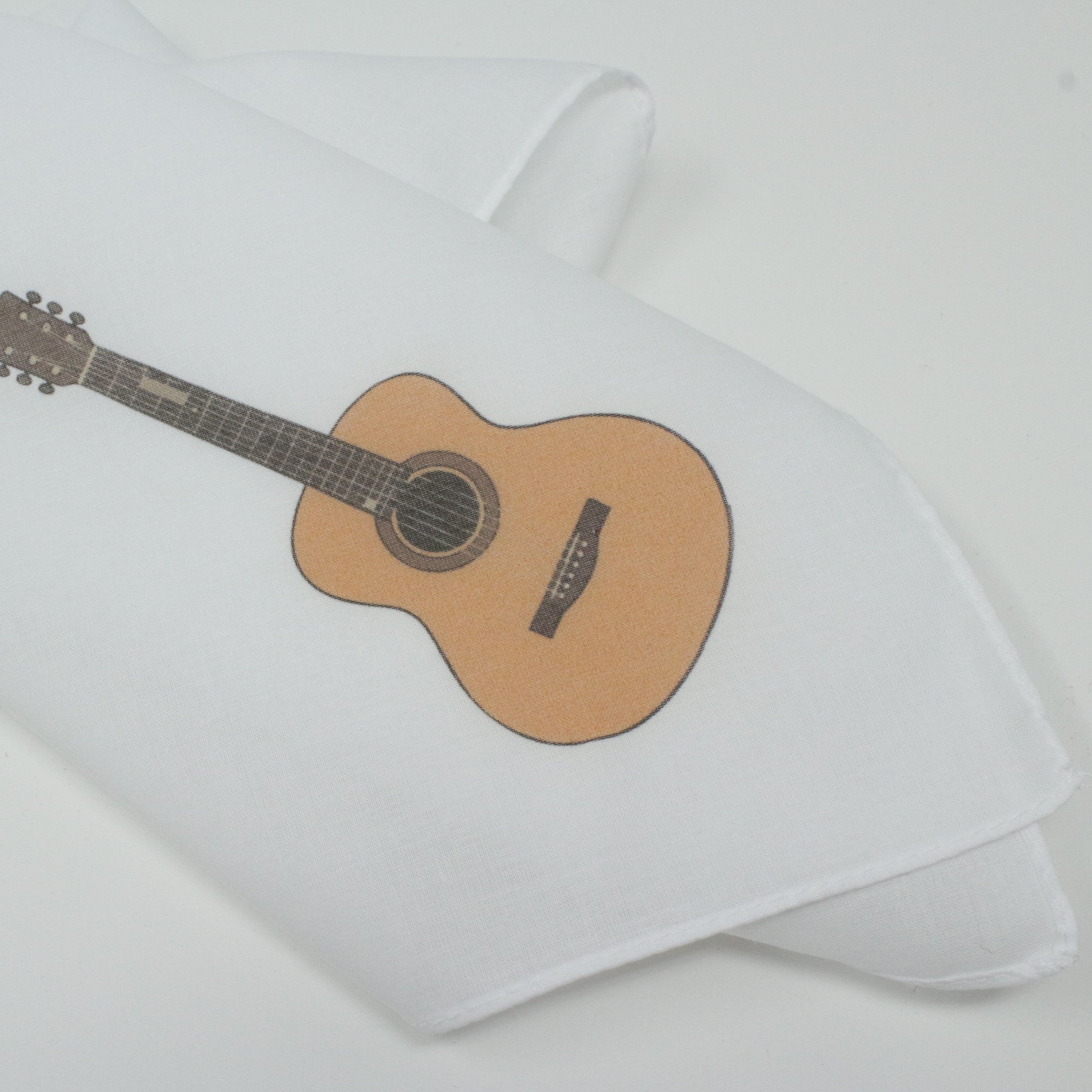 A folded white fabric item, likely a cotton hankie, printed with a graphic of an acoustic guitar in natural wood tones and black details, set against a clean white background.