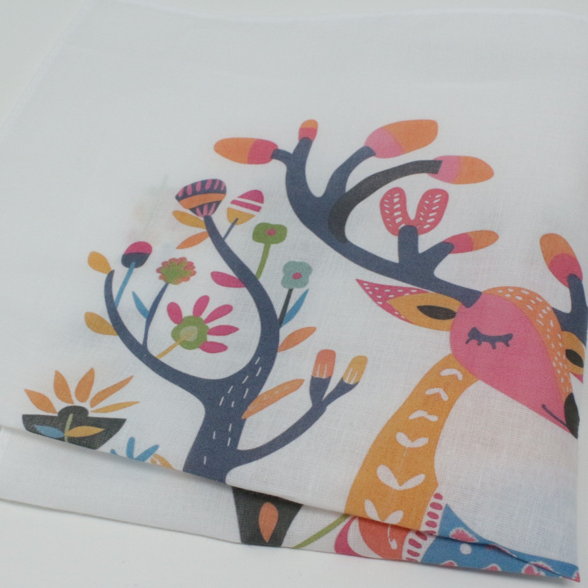A folded cotton handkerchief, featuring a whimsical colorful print of a deer and stylized trees.