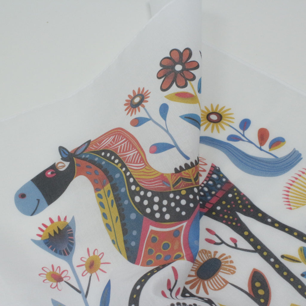 Cotton handkerchiefs. A close-up of a white surface printed with a whimsical folk-art horse design in multiple bright colors, including blue, red, yellow, orange, black, and white polka dots.