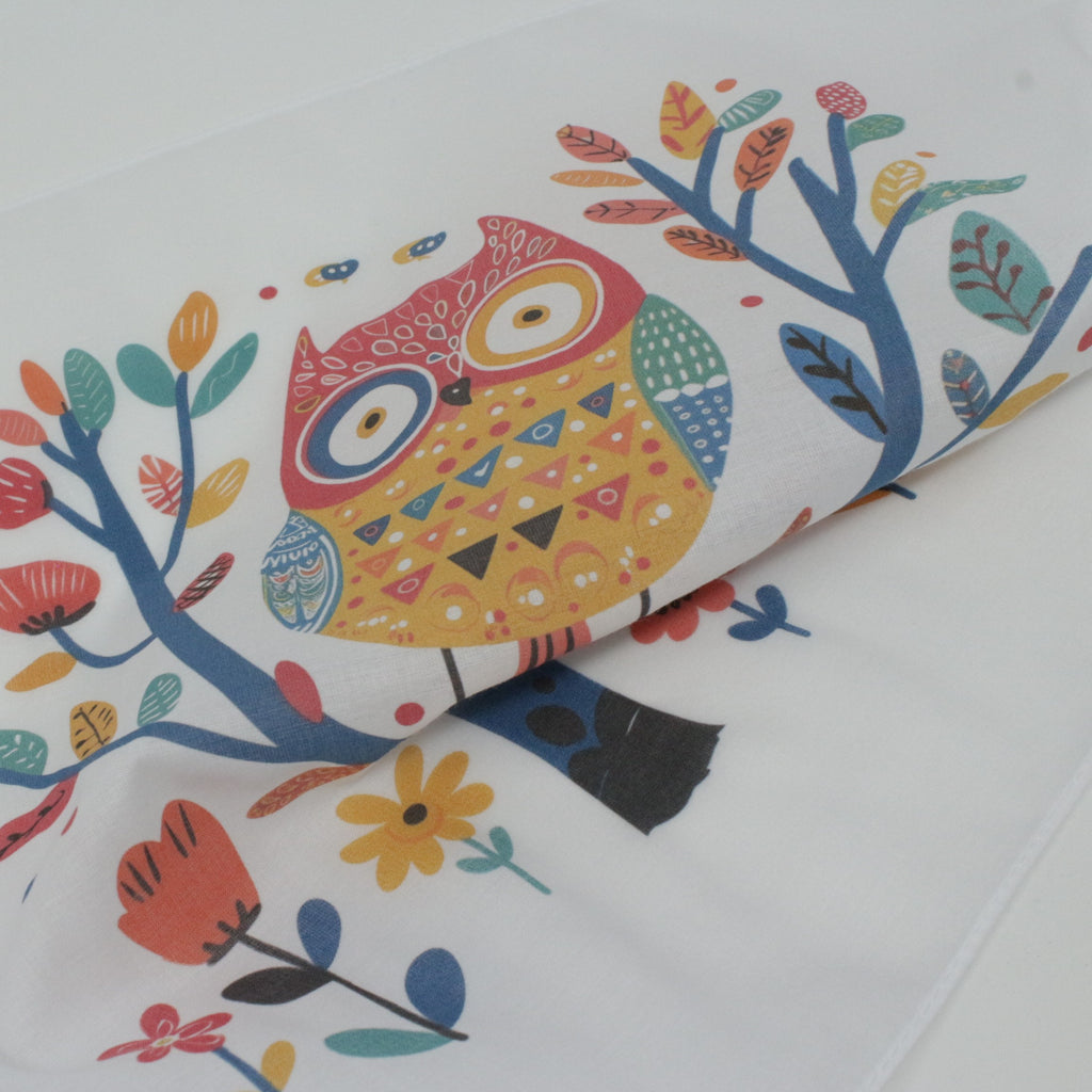A close-up of a white fabric cotton hankie pocket square, featuring a colorful printed design of an owl perched on stylized tree branches with flowers.